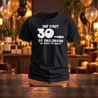 The First 30 Years of Childhood T-shirt in black on a wooden stand at a birthday party with gold and black balloons - funny 30th birthday gift