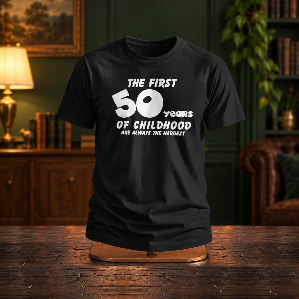 The First 50 Years of Childhood T-shirt in black on a wooden stand in a dark green room with a reading lamp - funny 50th birthday gift