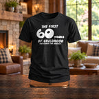The First 60 Years of Childhood T-shirt in black on a wooden stand by a stone fireplace - funny 60th birthday gift