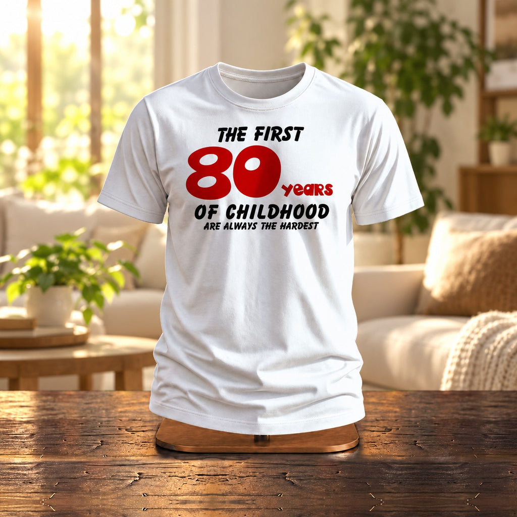 The First 80 Years of Childhood T-shirt in white with a red 80 on a wooden stand in a bright living room - funny 80th birthday gift