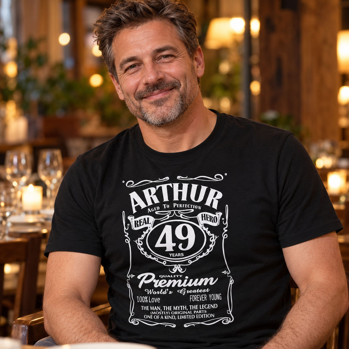 Personalised whisky label birthday t-shirt in black with name ARTHUR and age 49 - man at a restaurant table, personalised birthday gift for him