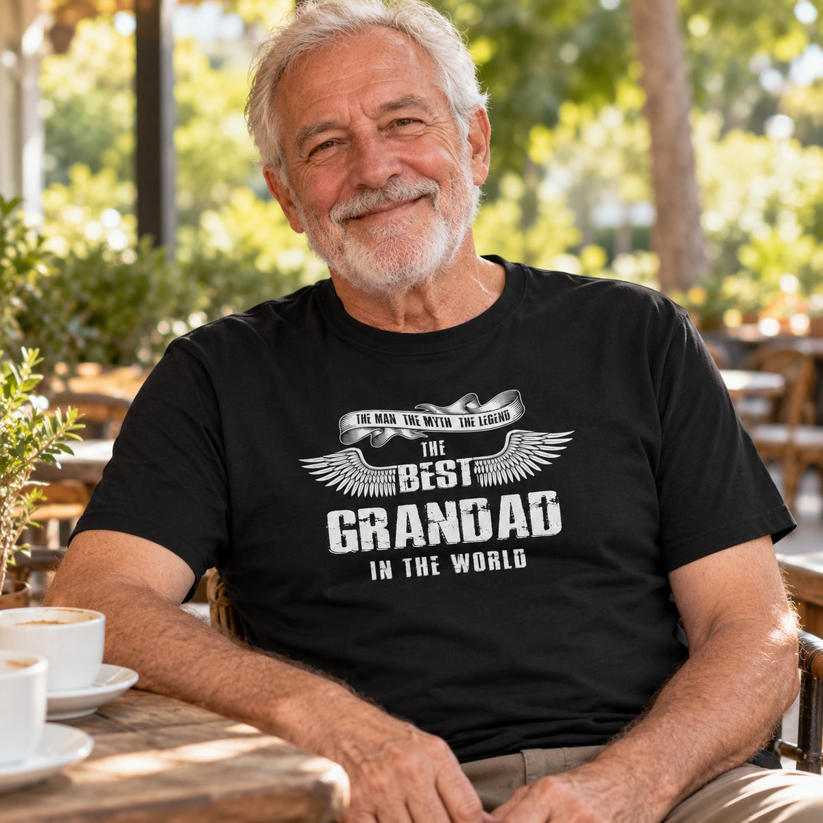 The Best Grandad In The World wings T-shirt in black - smiling grandad at a café table with a cup of coffee, gift for grandad
