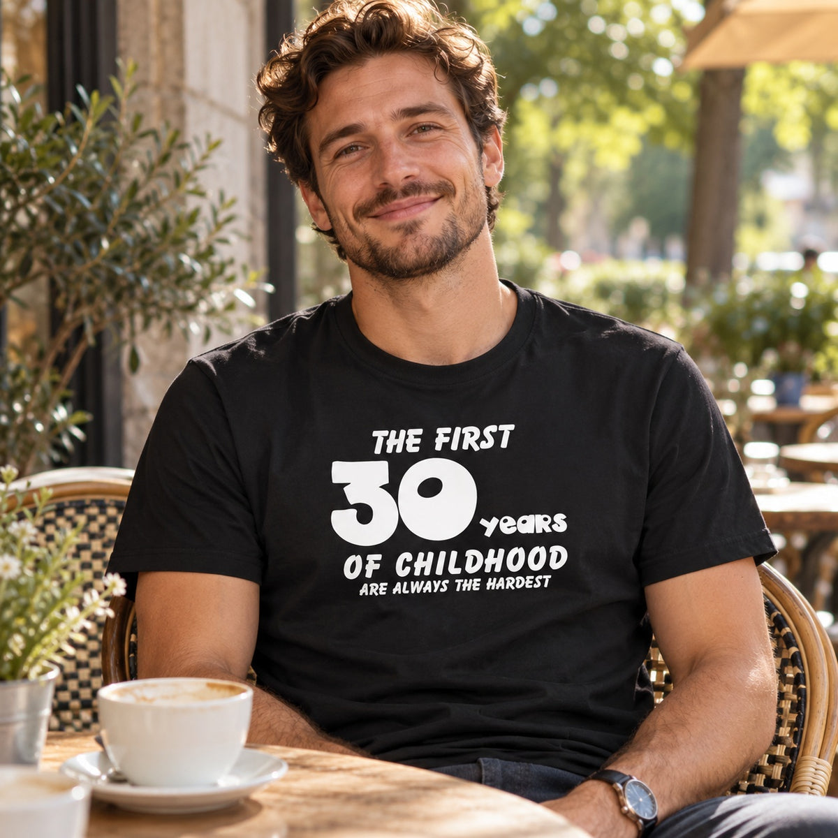 The First 30 Years of Childhood T-shirt in black - smiling man at a café table with a cup of coffee, 30th birthday gift