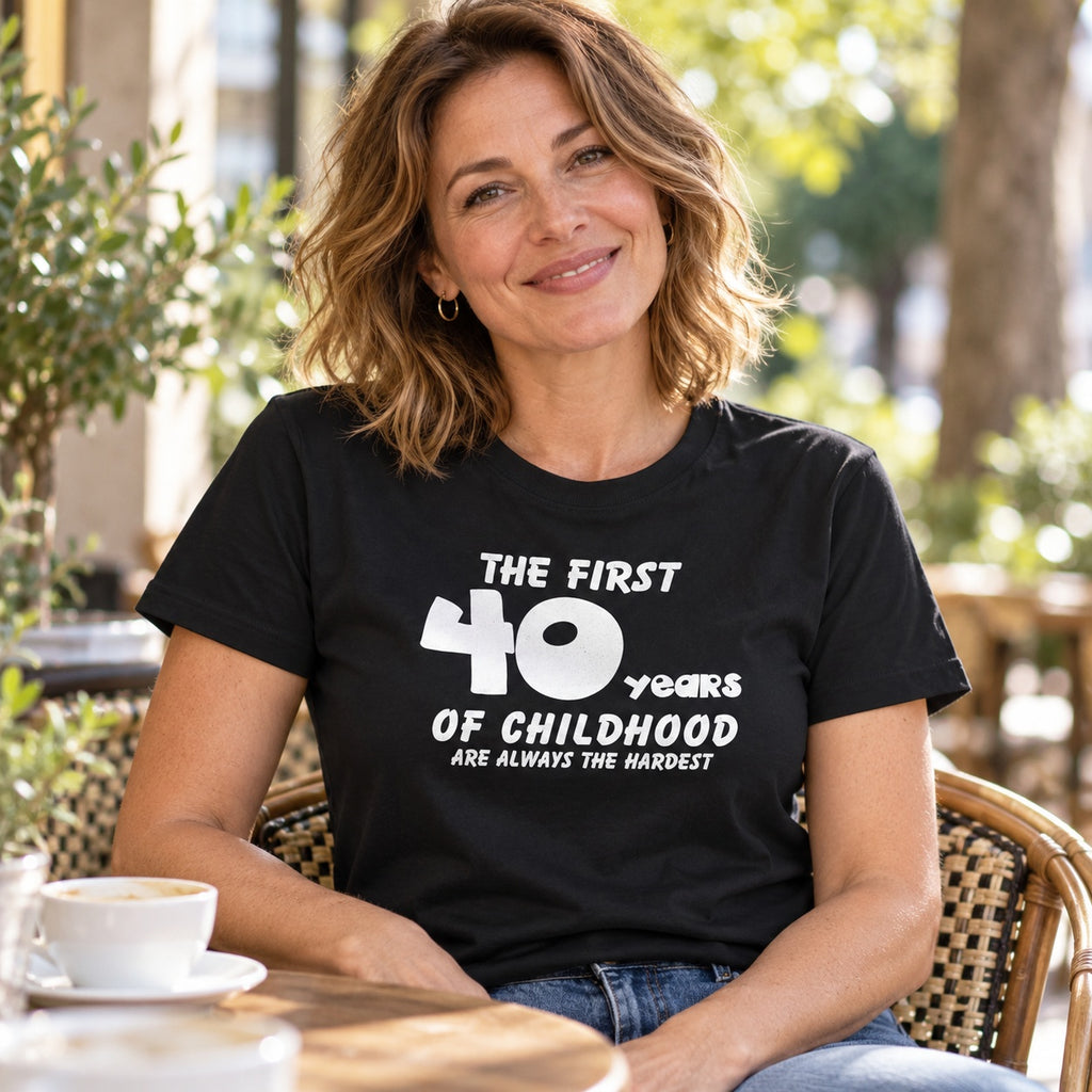 The First 40 Years of Childhood T-shirt in black - smiling woman at a café table with a cup of coffee, 40th birthday gift