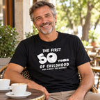 The First 50 Years of Childhood T-shirt in black - smiling man at a café table with a cup of coffee, 50th birthday gift
