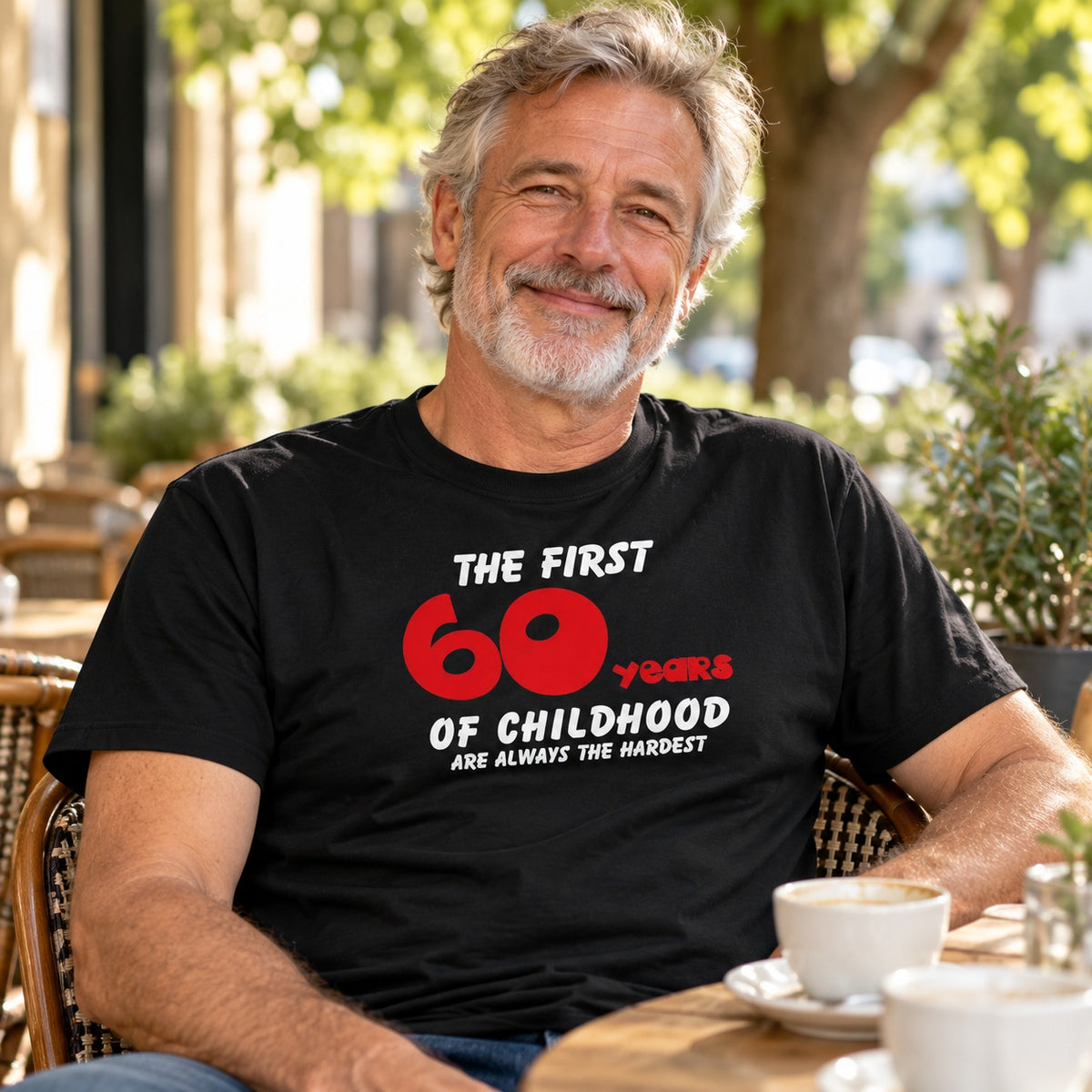 The First 60 Years of Childhood T-shirt in black with a red 60 - smiling grey-haired man at a café table, 60th birthday gift