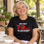 The First 70 Years of Childhood T-shirt in black with a red 70 - smiling woman at a café table with coffee, 70th birthday gift
