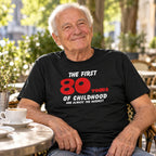 The First 80 Years of Childhood T-shirt in black with a red 80 - smiling older man at a café table with coffee, 80th birthday gift