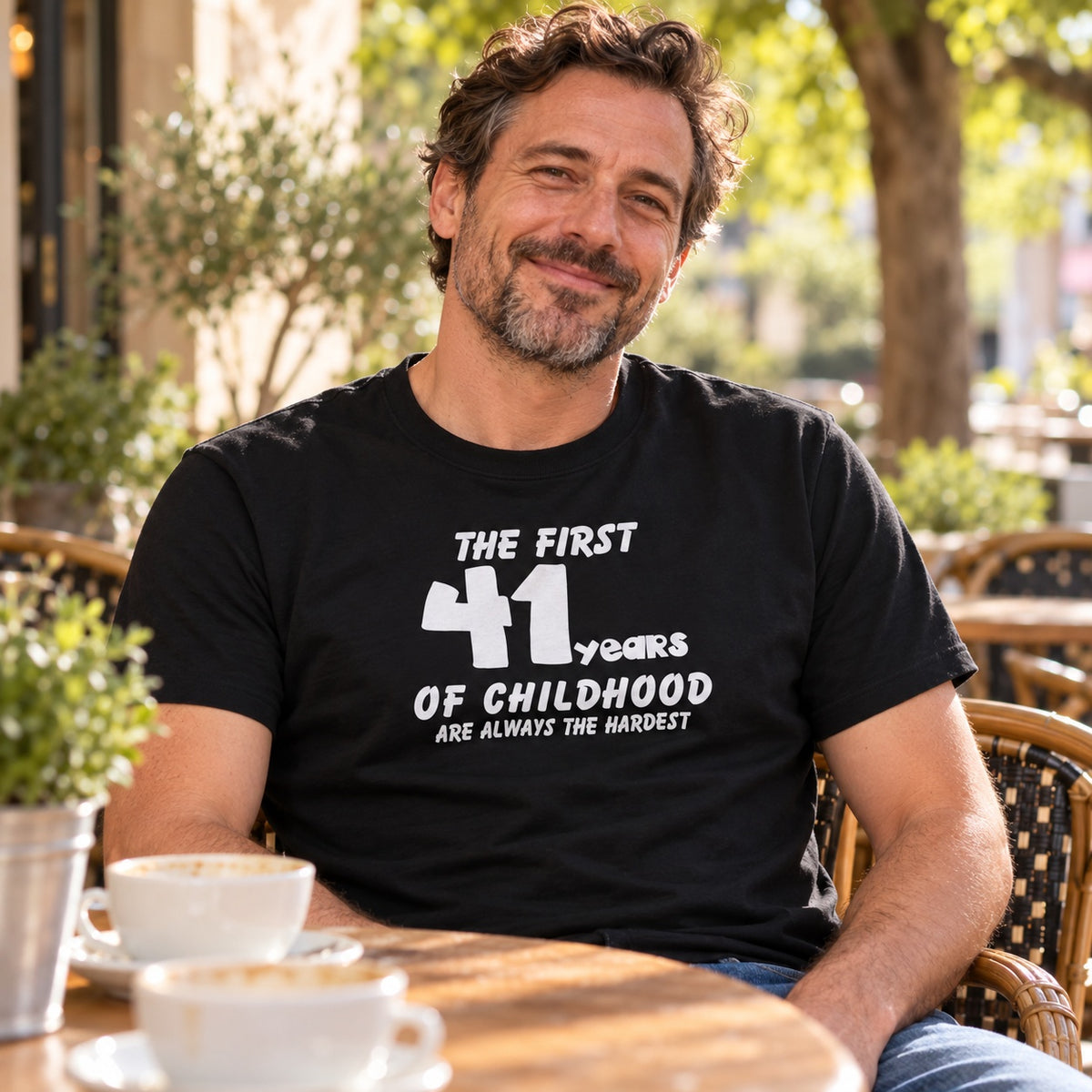 Personalised The First 41 Years of Childhood T-shirt in black - smiling man at a café table, example of a custom age birthday gift