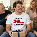 The First 30 Years of Childhood T-shirt in white with a red 30 - smiling man opening a birthday present with family, 30th birthday gift
