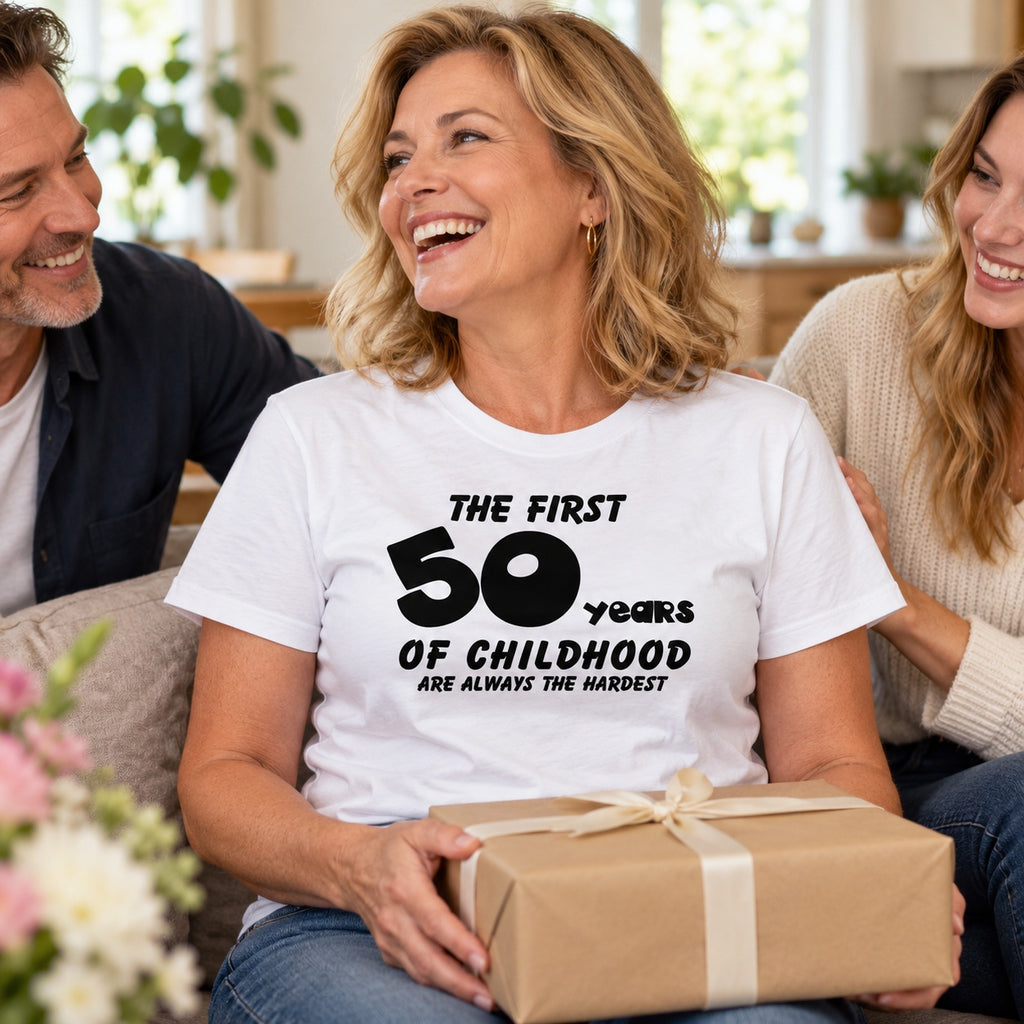 The First 50 Years of Childhood T-shirt in white - laughing woman opening a birthday present with family, 50th birthday gift