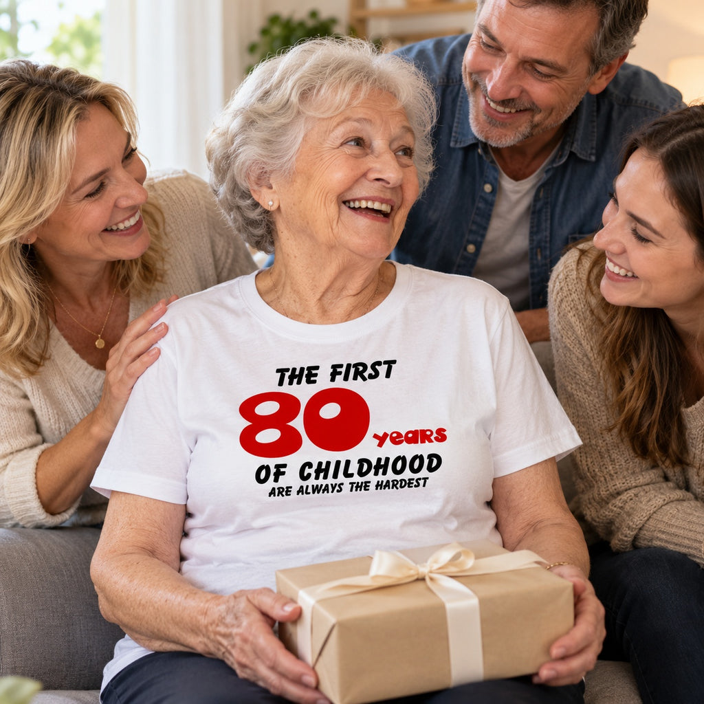 The First 80 Years of Childhood T-shirt in white with a red 80 - happy grandma holding a birthday present with her family, 80th birthday gift