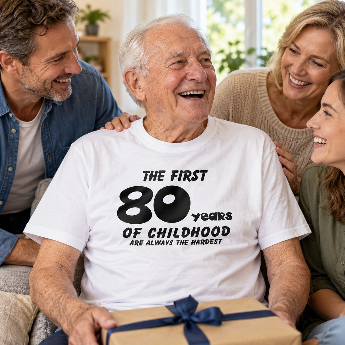 The First 80 Years of Childhood T-shirt in white - laughing man opening a birthday present with family, 80th birthday gift