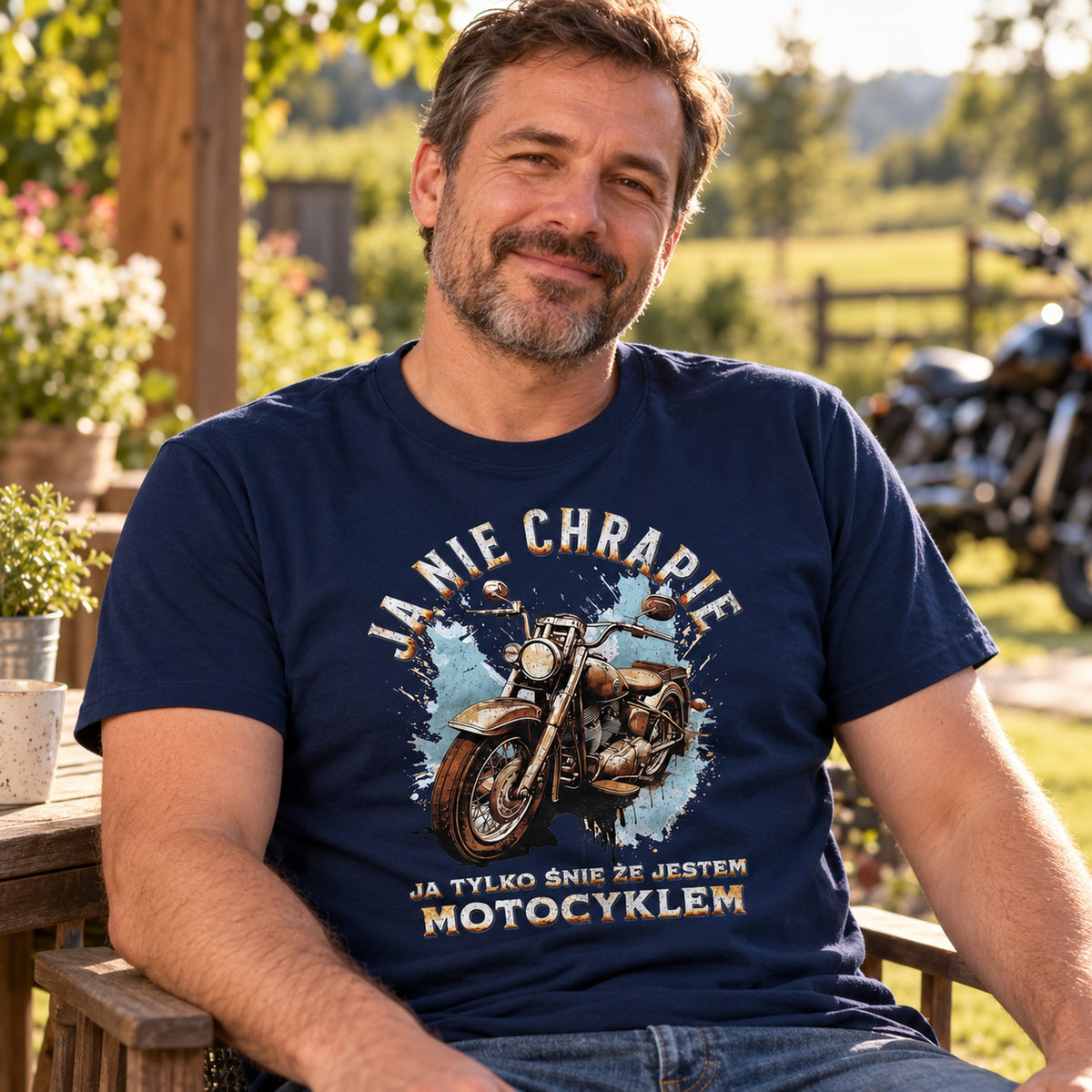Mężczyzna w granatowej koszulce „Ja Nie Chrapię, Ja Tylko Śnię, Że Jestem Motocyklem” na tarasie, w tle motocykl