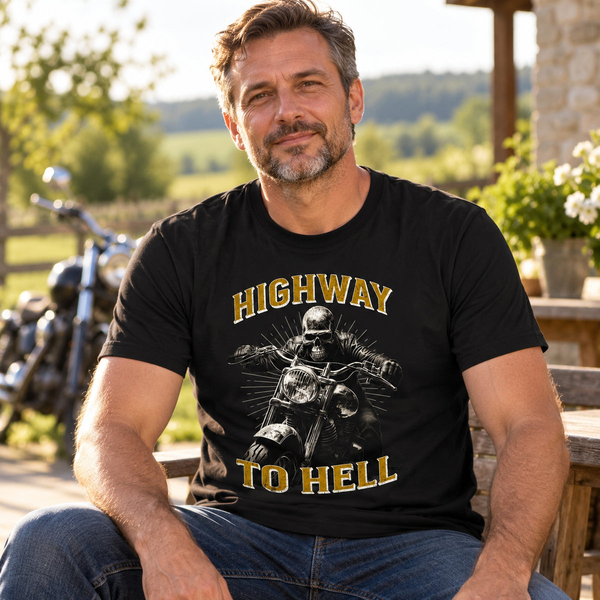 Biker in a black Highway to Hell skeleton biker (grey gold) t-shirt relaxing on a terrace, motorcycle in the background